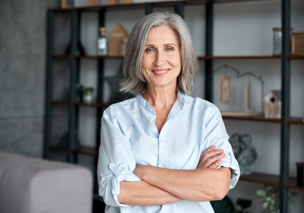 Confident older woman with grey hair and a warm smile, standing in a modern home – illustrating the ease of selling a mortgage note
