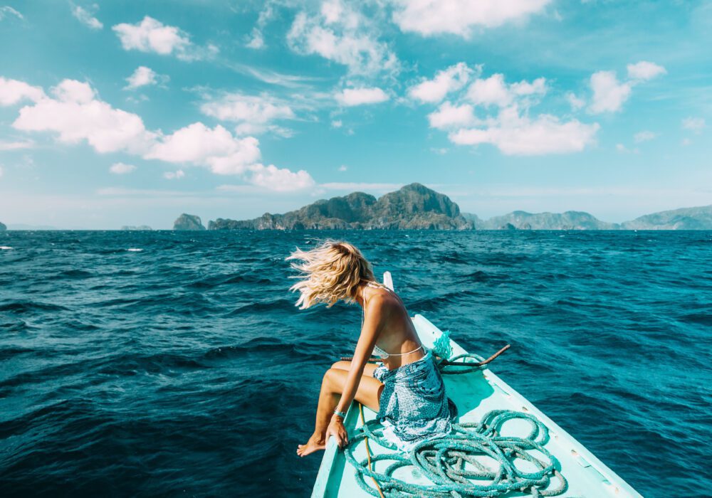 Woman sitting on the edge of a boat, hair in the breeze, looking out at tropical islands – representing the financial freedom of selling a mortgage note for a lump sum