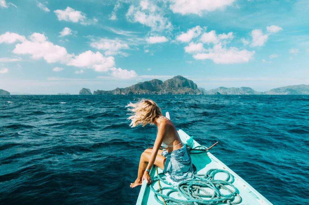 Woman sitting on the edge of a boat, hair in the breeze, looking out at tropical islands – representing the financial freedom of selling a mortgage note for a lump sum